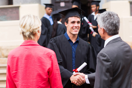 male graduate handshaking with his father at graduationの写真素材
