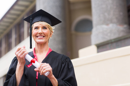 beautiful senior graduate holding certificate in front of university buildingの写真素材