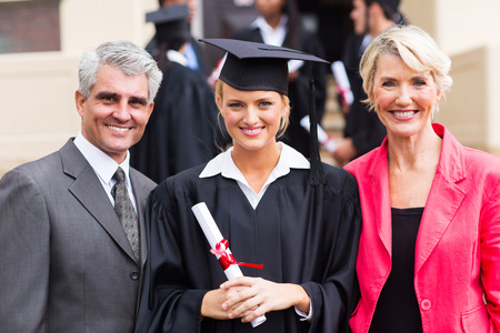smiling young female graduate with parents at graduation ceremonyの写真素材