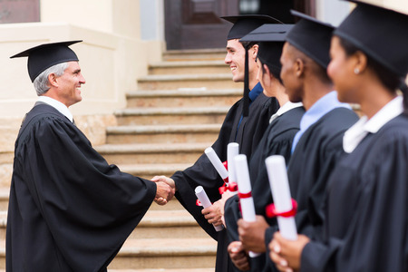 group of cheerful graduates in line handshaking with deanの写真素材