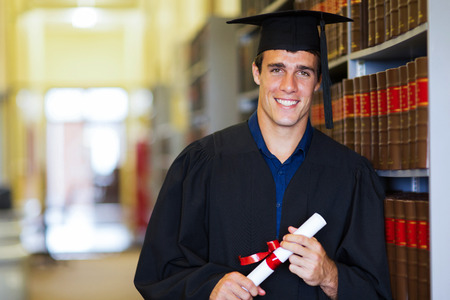 handsome male graduate wearing graduation gown in libraryの写真素材