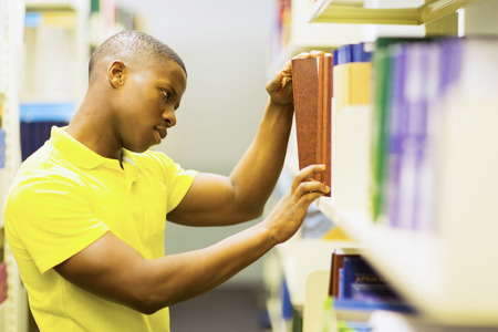 handsome male african college student looking for books in libraryの写真素材