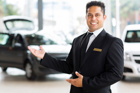 handsome indian salesman presenting new car to clients