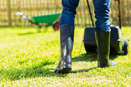 back view of man wearing gumboots mowing home garden lawn