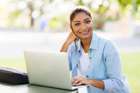 pretty indian university student using laptop computer outdoorsの写真素材