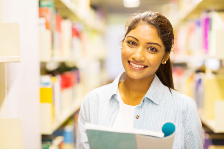 portrait of young indian college girl reading a book in libraryの写真素材