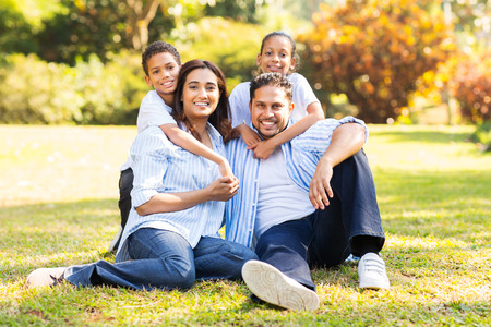 happy indian family sitting on grass in the parkの写真素材