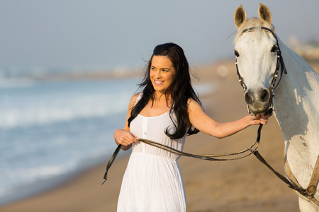 pretty young woman walking with a white horse on beach in early morningの写真素材