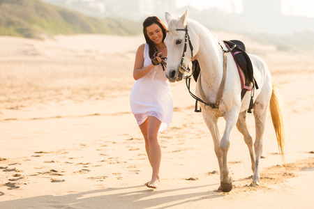 cheerful young woman walking with a horse on beach in early morningの写真素材