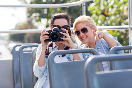 two playful tourists taking fun photos from an open top bus while touring the cityの写真素材