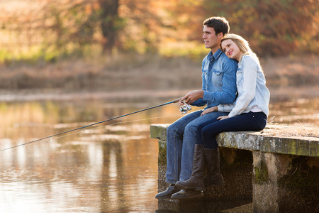 peaceful young couple fishing by the pond in autumnの写真素材