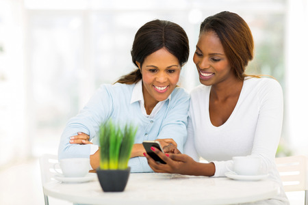 beautiful african mother and daughter using smart phone at homeの写真素材