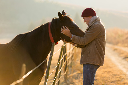 caring young man touching his horses in winter morningの写真素材