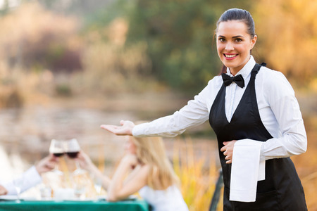 pretty young waitress welcomes customers to romantic dinning environmentの写真素材
