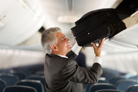 mature businessman putting luggage into overhead locker on airplaneの写真素材