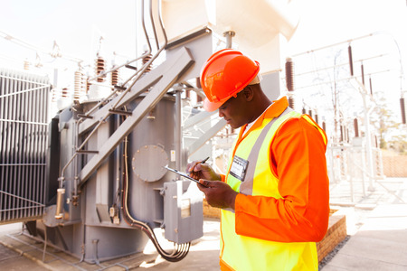 handsome afro american electrical engineer writing on clipboard in power plant