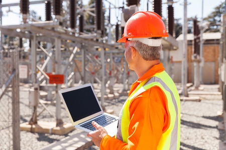 senior technician holding laptop computer in substation
