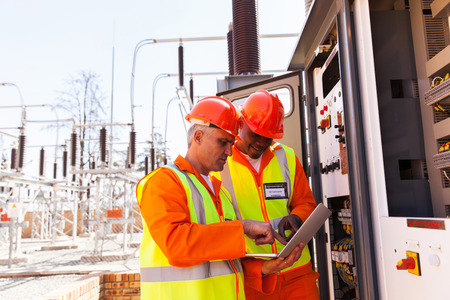 two electrical engineers using laptop computer next to transformer