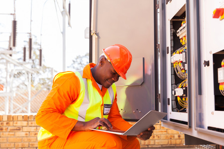 handsome african electrical engineer working on laptop next to transformerの写真素材