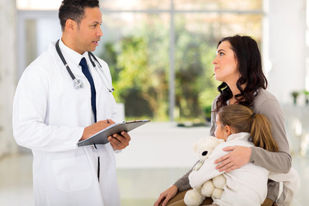 friendly male paediatrician consulting young girl and mother in hospitalの写真素材