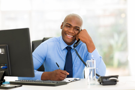 cheerful african american businessman talking on phone in the officeの写真素材