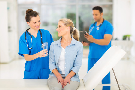 caring young medical intern offering senior patient waterの写真素材