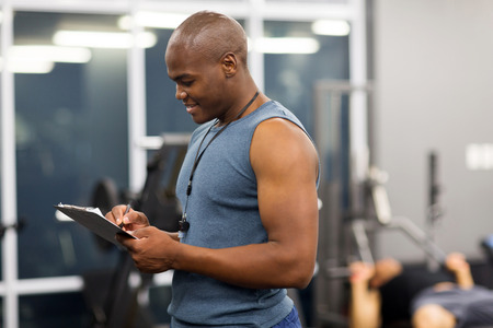 side view of african male gym instructor writing on clipboardの写真素材