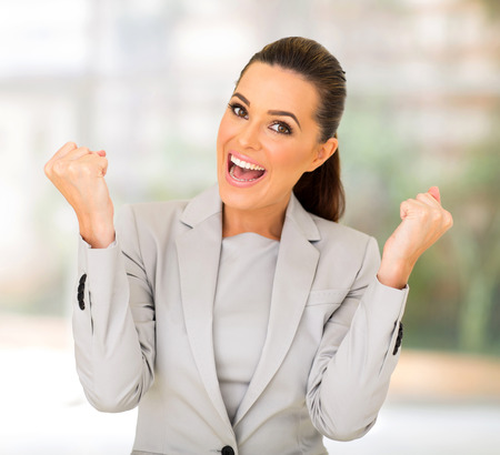 excited businesswoman waving fists in officeの写真素材