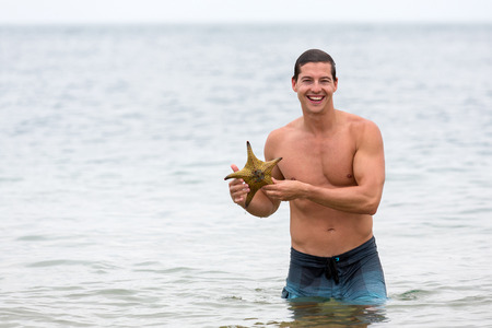 young man in water holding a starfishの写真素材