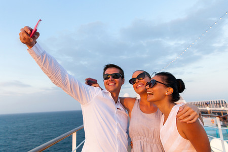 group of friends taking self portrait using smart phone on cruiseの写真素材