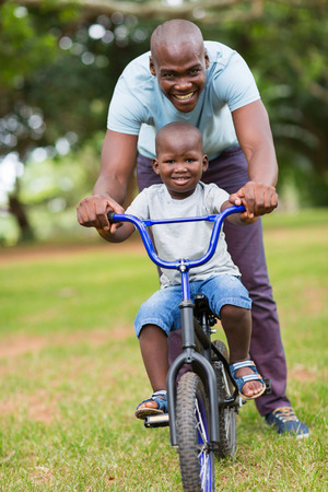 cheerful african american man teaching son to ride a bicycle at the parkの写真素材