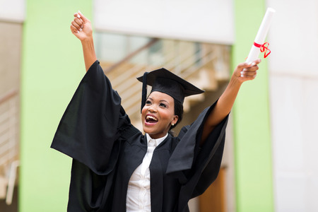 cheerful afro american female graduate standing in front of university building