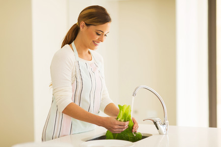 happy young woman washing lettuce in the kitchenの写真素材