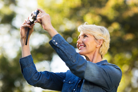 happy mature woman using a camera to take photo outdoors at the parkの写真素材
