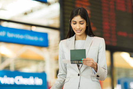 young businesswoman looking at boarding pass in front of flight information board at airportの写真素材