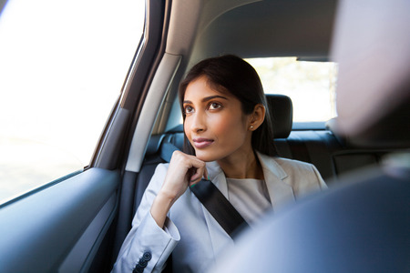 elegant young indian businesswoman sitting in car backseatの写真素材
