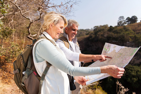 active senior hikers on top the mountain pointing at map