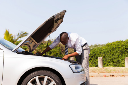 afro american man looking at broken down car engine by side of the roadの写真素材
