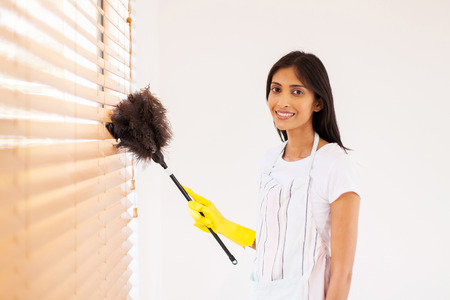 pretty young indian woman cleaning window blinds with feather duster