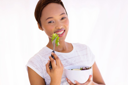 close up portrait of healthy young african woman eating green salad at homeの写真素材