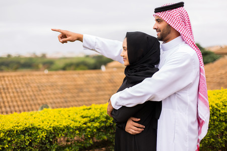 cheerful young middle eastern couple pointing outside their house