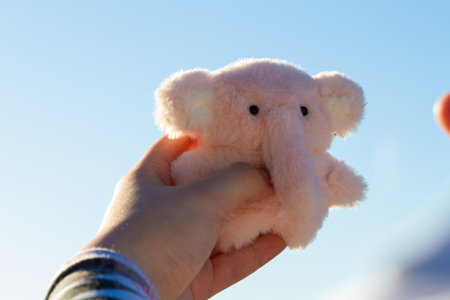 Cute pink elephant plush held against a clear blue sky during a sunny day