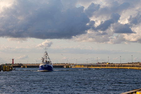 Boat navigates through harbor with cloudy skies in the background during late afternoon at the coastlineの写真素材