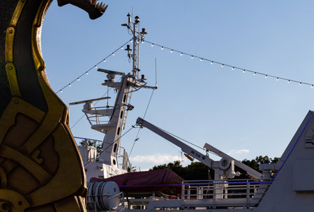Coastal view with ships deck, masts, and overhead lights during sunset at the marina