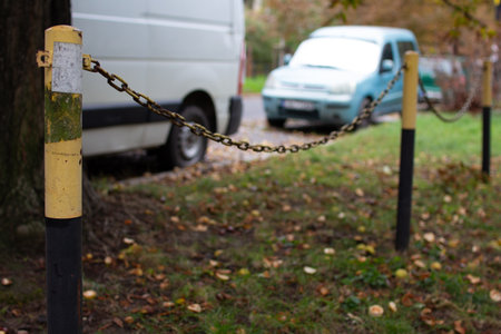 Chain link barrier marks off grassy area beside parked vehicles during autumn afternoon in a quiet...