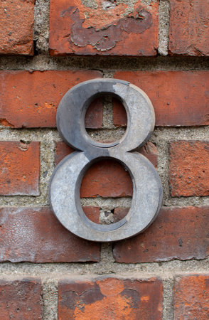 Stylish metal number eight affixed to a weathered brick wall in an urban settingの写真素材