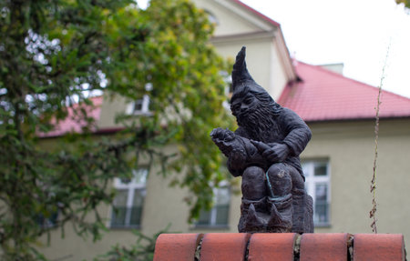 Small bronze gnome sculpture sits on a wall next to a historic buildingの写真素材