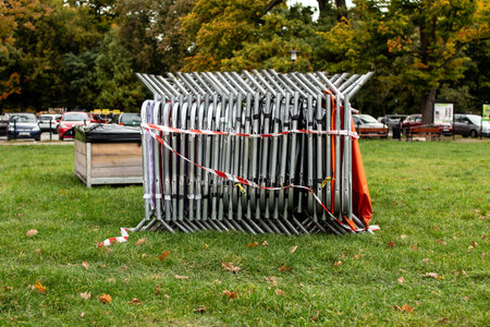 Event barriers are stacked neatly in a park during autumn with parked carsの写真素材
