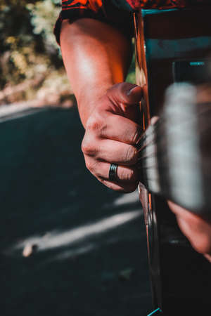 A hand clenched into a fist ready to hit the strings of a guitar. A ring is dressed on the ring...