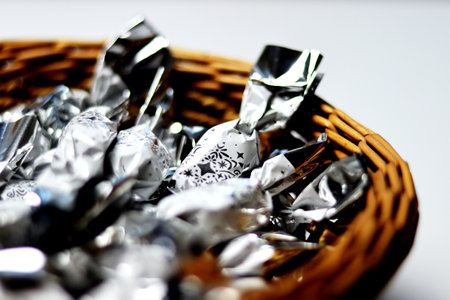 Close up of white and silver packaged Christmas chocolate candies in a brown wicker basket on a white background - macro photographyの写真素材